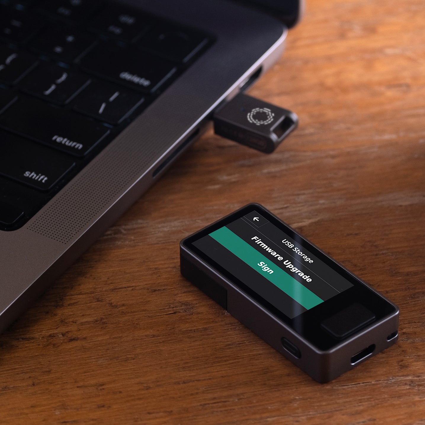 Blockstream Jade Plus Bitcoin hardware wallet beside laptop, USB-C adapter plugged in, screen showing firmware-upgrade prompt